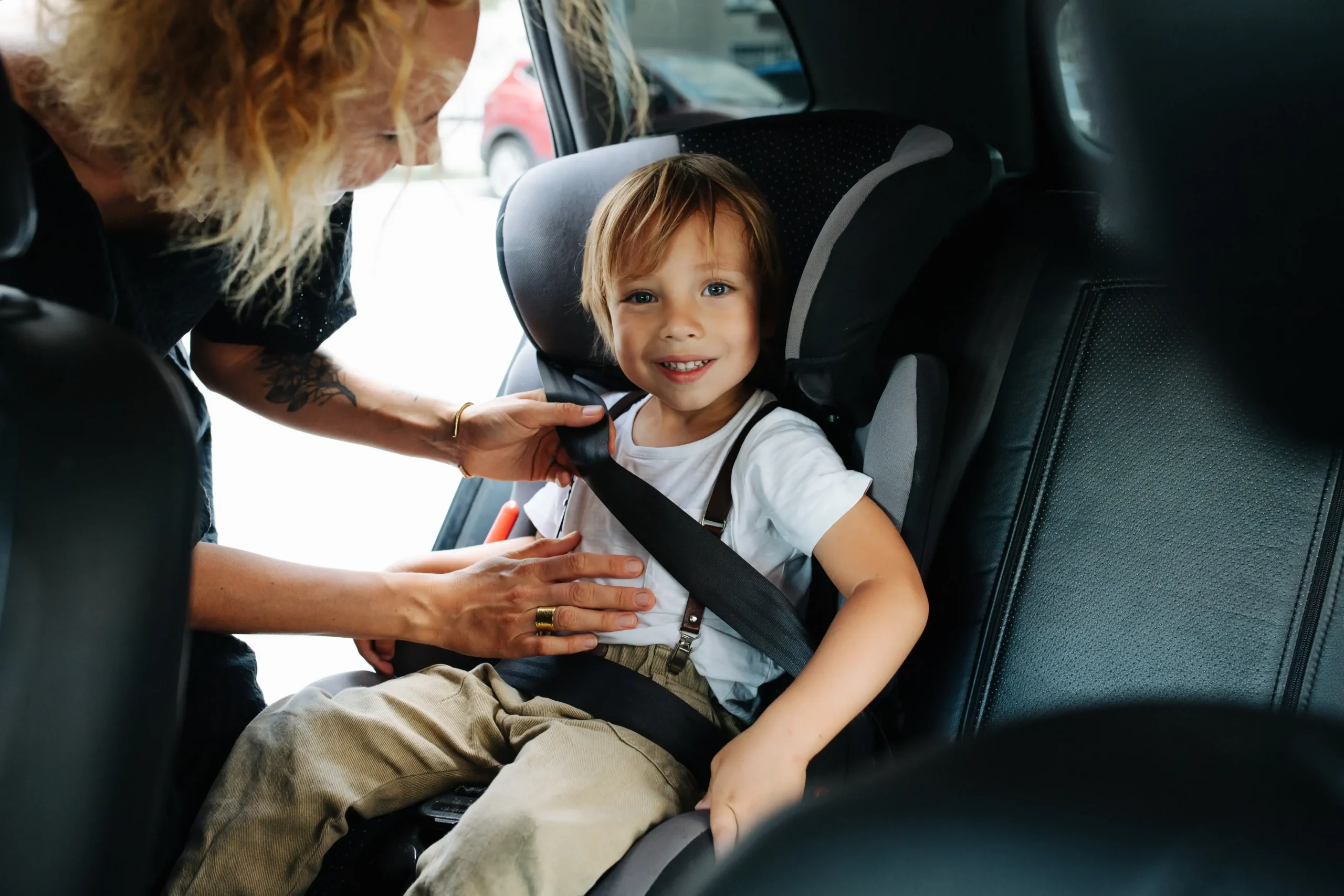 mãe a colocar o filho, criança, na sua cadeira no carro com cinto de segurança